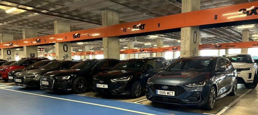 Row of parked midsize rental cars at a Sixt location inside a covered garage.