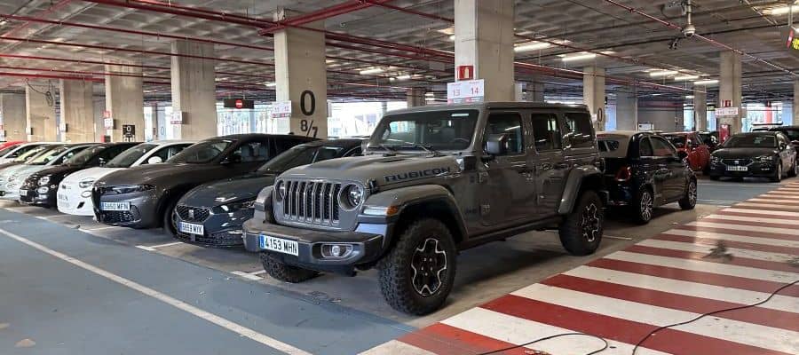 A rugged Jeep Wrangler Rubicon parked slightly over the striped pedestrian walkway in a covered parking garage