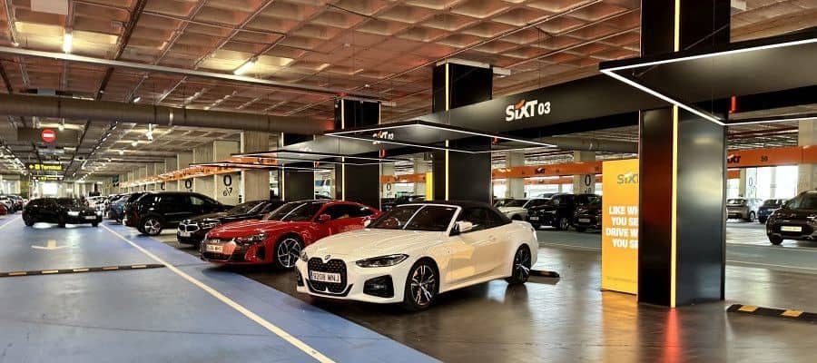 White BMW convertible parked in a premium Sixt rental zone inside a modern airport garage, ready for customer pickup