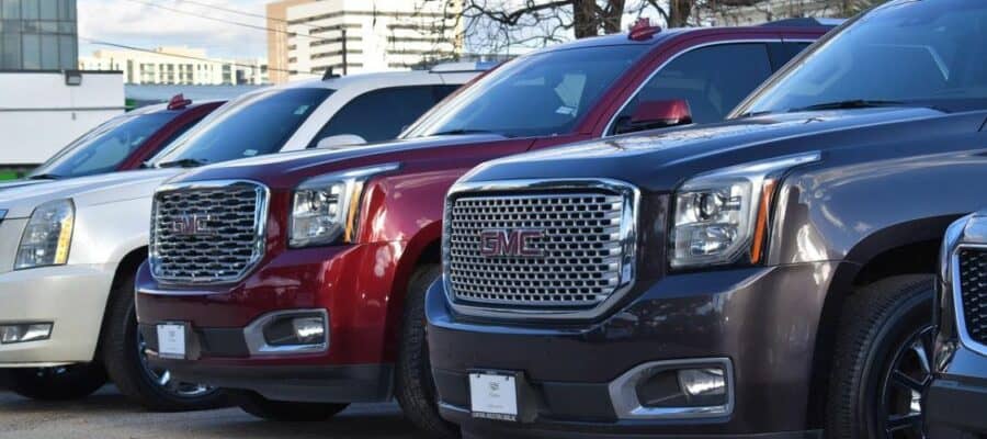 Row of full-size SUVs, including GMC Yukon models, lined up on a Sixt parking lot, featuring chrome grilles and bold front-end styling.
