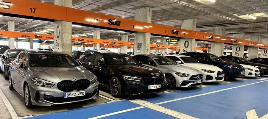 A row of premium sedans from BMW, Mercedes, Audi, and others parked at a Sixt rental return area in a covered garage
